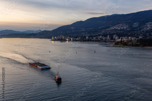 West Vancouver, British Columbia, Canada. Aerial View of a Tugboat in a modern cityscape on the Pacific Ocean Coast during an Autumn sunny and cloudy sunset.