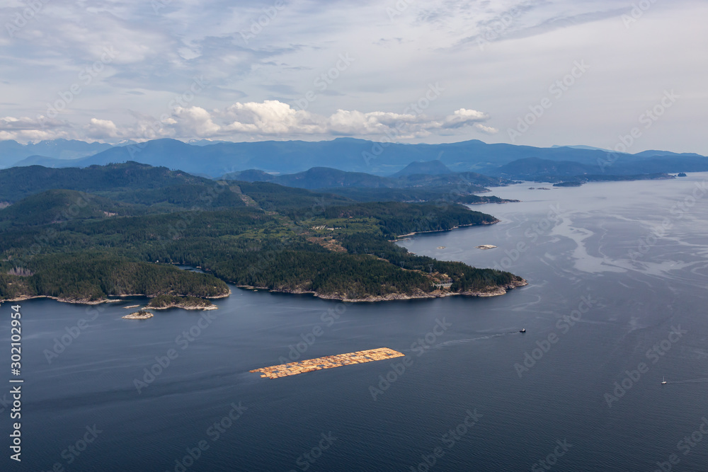 Aerial View of Tugboat towing Lumber in the ocean with mountain landscape in the background during a hazy summer day. Taken in Sunshine Coast, BC, Canada.