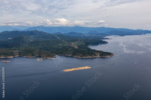 Aerial View of Tugboat towing Lumber in the ocean with mountain landscape in the background during a hazy summer day. Taken in Sunshine Coast, BC, Canada.