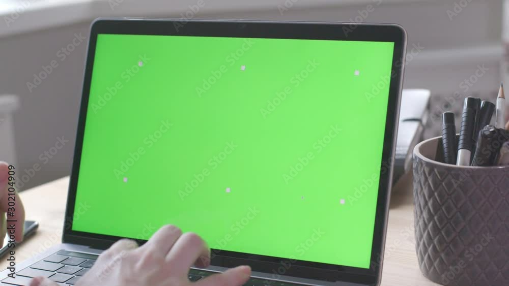 Over the shoulder shot of young woman working on modern laptop with green screen mock-up. Hands on keyboard. Over the shoulder shot of young woman working on modern laptop with green screen mock-up. Hands on keyboard.