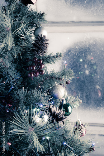 Christmas tree decorated with balls and lights reflected on a frost covered window.