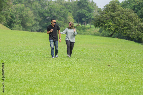 Young playful young muslim Asian couple  running together hand by hand on natural background © SVRSLYIMAGES