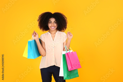 Beautiful African-American woman with shopping bags on color background © Pixel-Shot