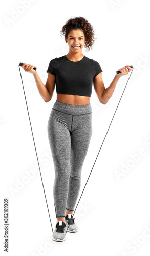 Sporty African-American woman with jumping rope on white background