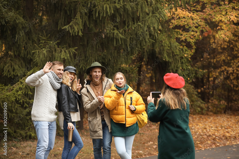 Young woman taking photo of her friends in autumn park