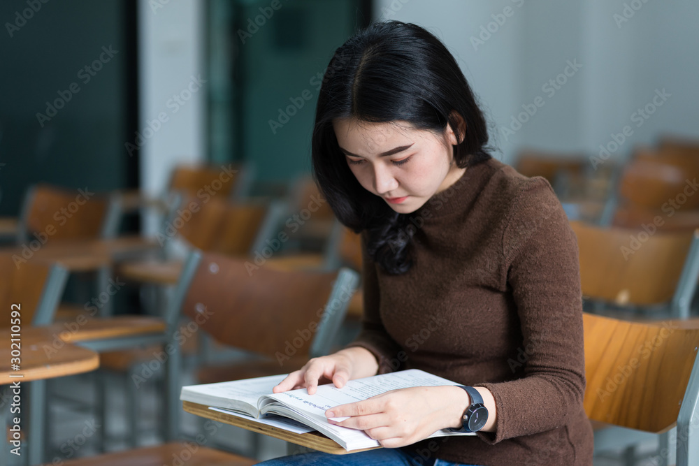 A teenager woman university student sits on wooden a chair concentrates reading textbook in the classroom preparing for examination. A teenager woman university student sits on wooden a chair concentrates reading textbook in the classroom preparing for examination.