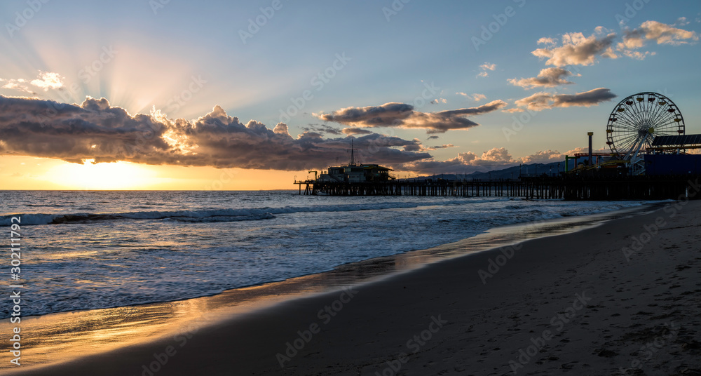 Silhouette of the Santa Monica Pier in California as the sun sets turning the ocean gold.