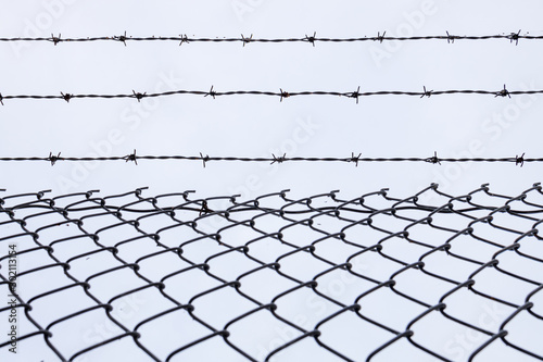 Chainlink fence with three strands of barbed wire on top. Close up and isolated against the sky