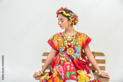 Mexican girl with a floral dress from Oaxaca Mexico, hidden in a red background with braided flowers and gold necklaces, for Mexican culture dance