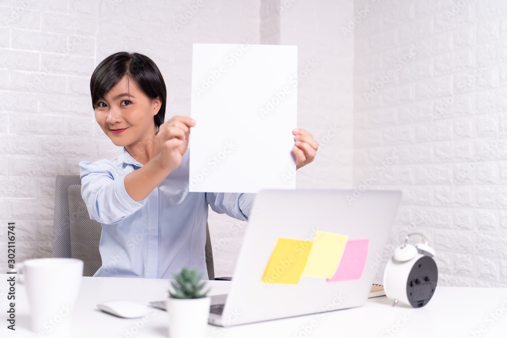 Happy woman sitting at home office and showing blank sheet Happy woman sitting at home office and showing blank sheet