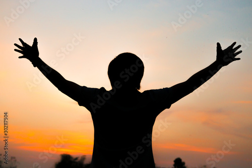 Silhouette of a man with hands raised in the sunset