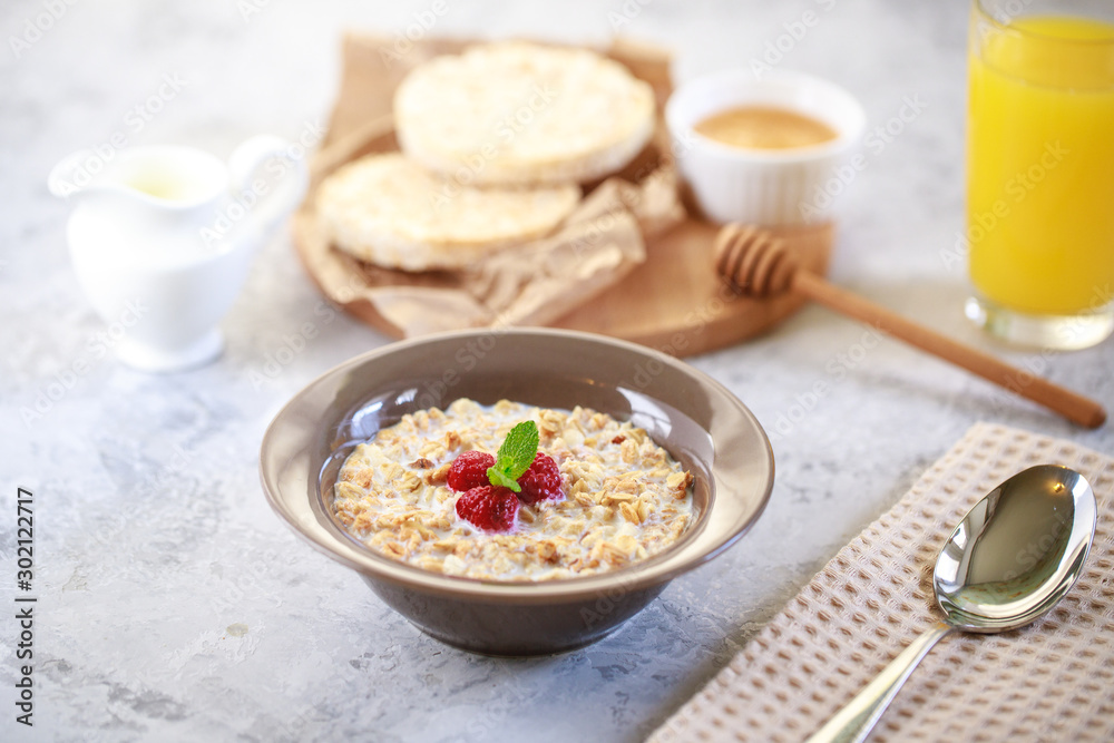 A healthy and dietary breakfast. Baked granola with milk and raspberries in a plate, whole grain breads and freshly squeezed juice. Delicious muesli.