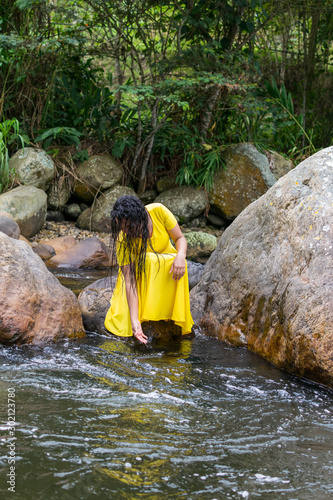 beautiful woman in yellow dress touching the river water