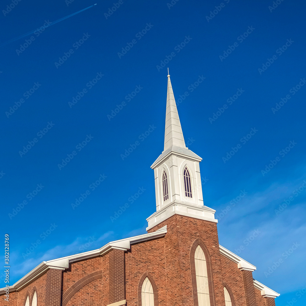 Square frame Sunny day view of a church with white steeple and vibrant blue sky background