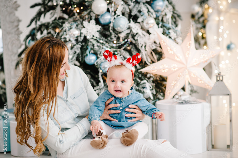 Baby girl with mom on floor near Christmas tree. Happy New Year and Merry Christmas. Christmas decorated interior. The concept of family holiday. Baby girl with mom on floor near Christmas tree. Happy New Year and Merry Christmas. Christmas decorated interior. The concept of family holiday.