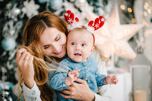 Baby girl with mom on floor near Christmas tree. Happy New Year and Merry Christmas. Christmas decorated interior. The concept of family holiday.