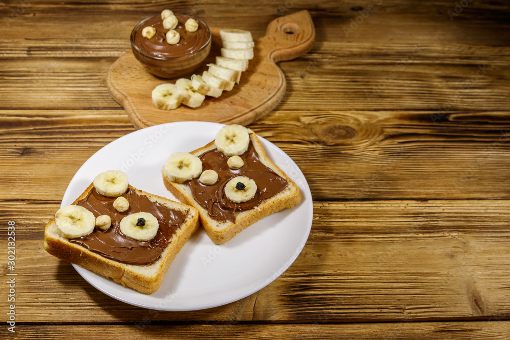 Two sweet sandwiches with delicious chocolate hazelnut spread and banana in shape of bear on wooden table Two sweet sandwiches with delicious chocolate hazelnut spread and banana in shape of bear on wooden table