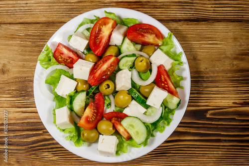 Greek salad with fresh vegetables, feta cheese and green olives on wooden table. Top view