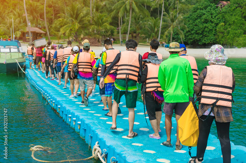 Group of tourists walking on plastic pontoon walk way floating in the sea go to the beach. photo