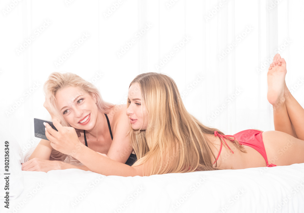 Obraz premium In the bedroom, in the white bed, in the morning, women wearing two black and red bikinis, playing fun with their mobile phone.