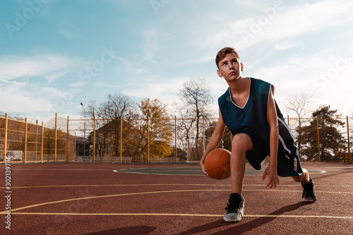SSports and basketball. A young teen in a black tracksuit playing basketball on the school Playground. Copy space © _KUBE_