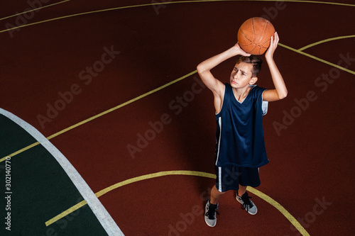 Sports and basketball. A young teenager in a blue tracksuit throws a jump ball into the basket. Ground on the background