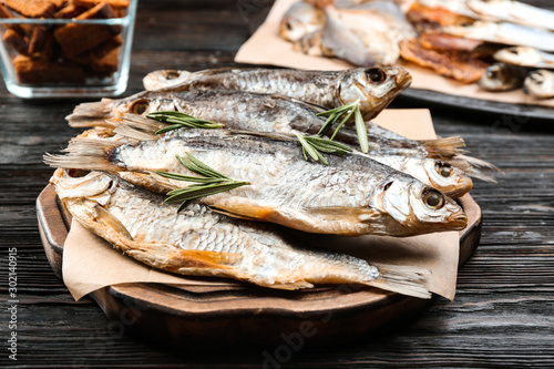 Tasty dried fish with rosemary on black wooden table