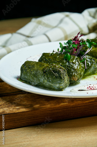 Traditional georgian dolma in grape leaves staffed with rice and meat on white plate on wooden background. CLose up. Selective focus.