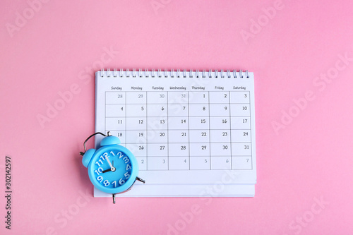 Calender and alarm clock on pink background, flat lay photo