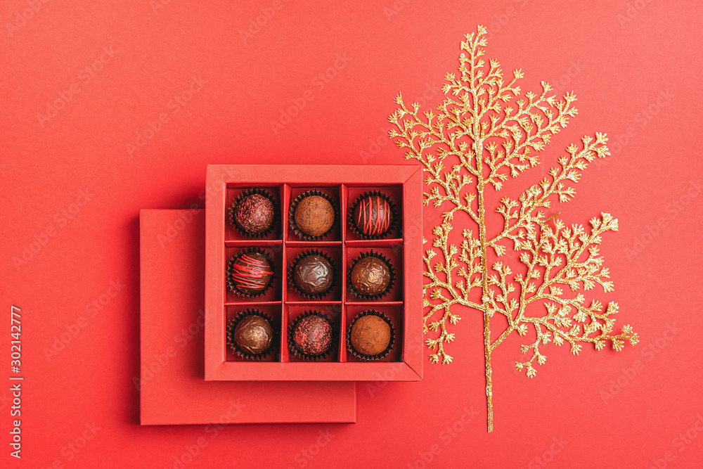 Chocolate candies in a red craft box golden branch of plant on a bright coral background. Flat layout . Holiday Concept Chocolate candies in a red craft box golden branch of plant on a bright coral background. Flat layout . Holiday Concept