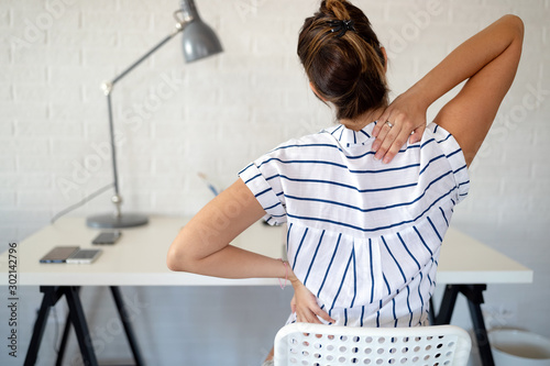 Overworked woman with back pain in office with bad posture photo