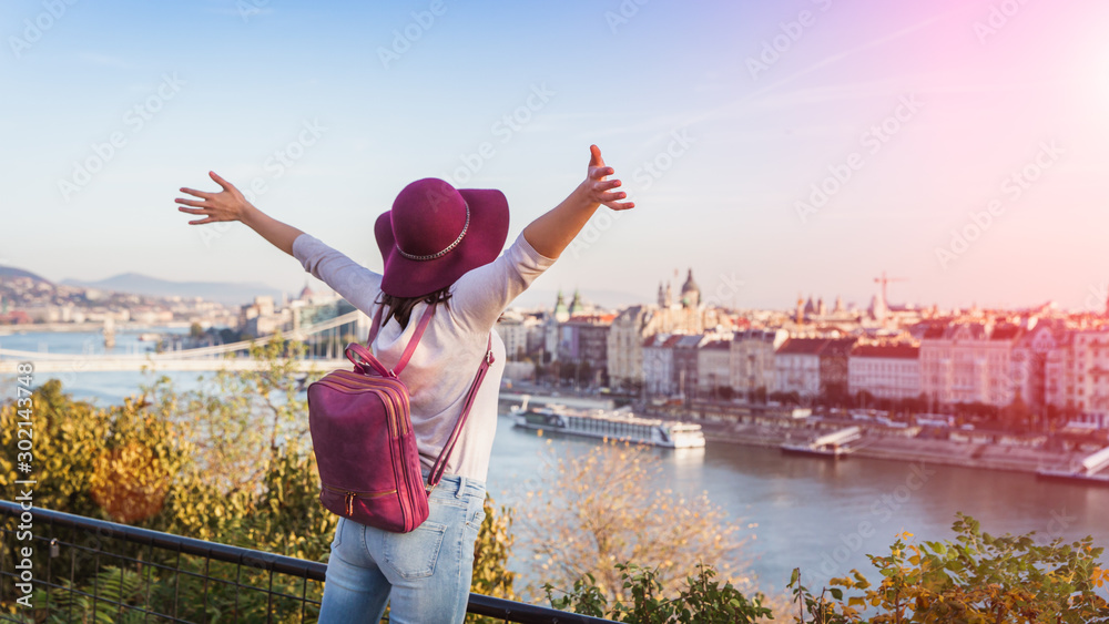 Naklejka premium A happy young woman enjoying her trip to Budapest, Hungary from the point from Gellert Hill during sunrise in autumn during sunrise.