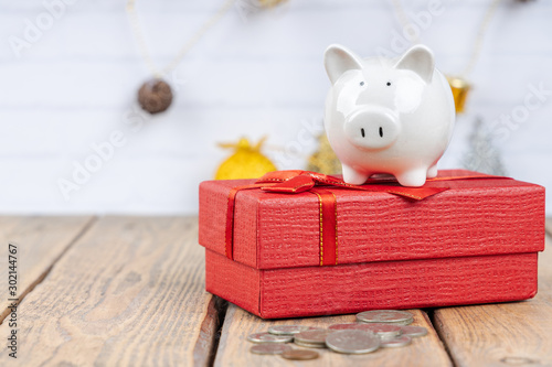 Piggy bank with coins and red gift box on wooden background. Festive and financial concepts