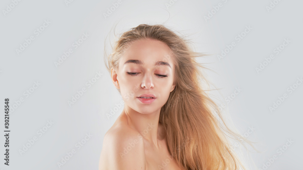 Portrait of beauty model with natural nude make up and touching her face. Spa, skincare and wellness. Close up, Gray background, copyspace. hair fluttering in the wind. - obrazy, fototapety, plakaty 