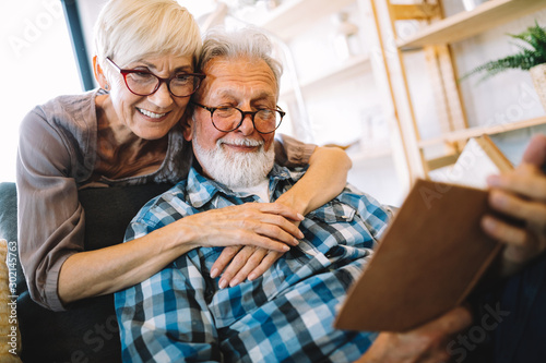 Beautiful old couple is reading a book and smiling at home photo