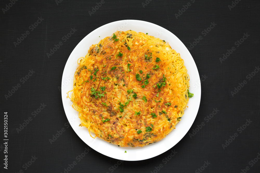 Homemade spaghetti omelette on a white plate on a black surface, top view. Flat lay, overhead, from above. Homemade spaghetti omelette on a white plate on a black surface, top view. Flat lay, overhead, from above.