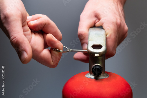 Actions in case of fire. Pull the safety pin out of the fire extinguisher by the ring. Men's hands close-up. Safety measures in the office and in the workplace. Emergency Prevention. Grey background.