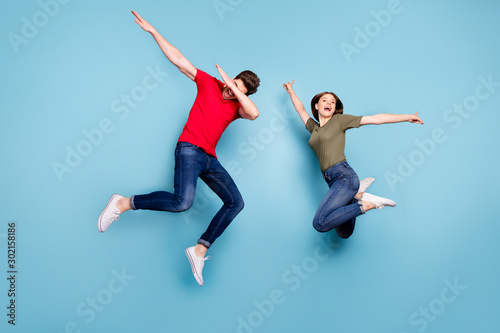 Full size photo of funky crazy two married people students fun jump man perform dab dancers woman raise hands wear green red t-shirt denim jeans sneakers isolated blue color background