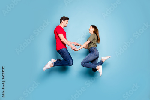 Full body profile side photo of charming two spouses relax rest on spring holidays jump hold hands feel content wear casual style clothes isolated over blue color background