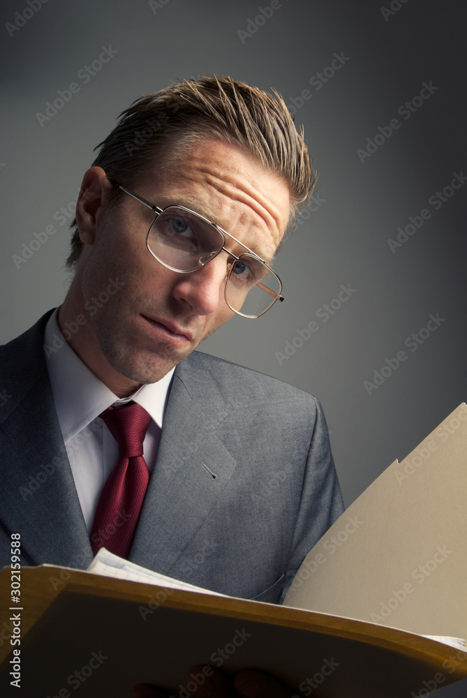 Skeptical businessman holding a file folder looking at the camera with a serious expression Skeptical businessman holding a file folder looking at the camera with a serious expression
