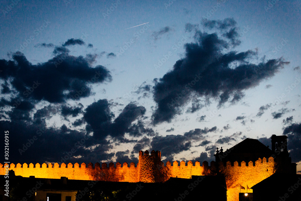 Campanario sobre muralla medieval al atardecer con nubes