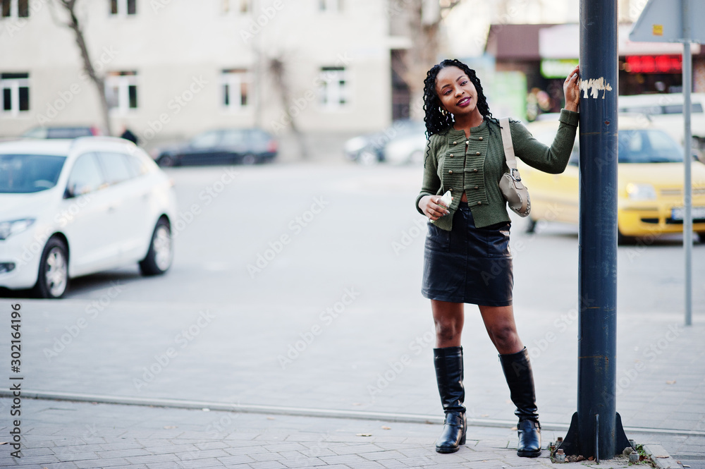Stylish fashionable african american women in green sweater and black skirt posed outdoor with mobile phone.