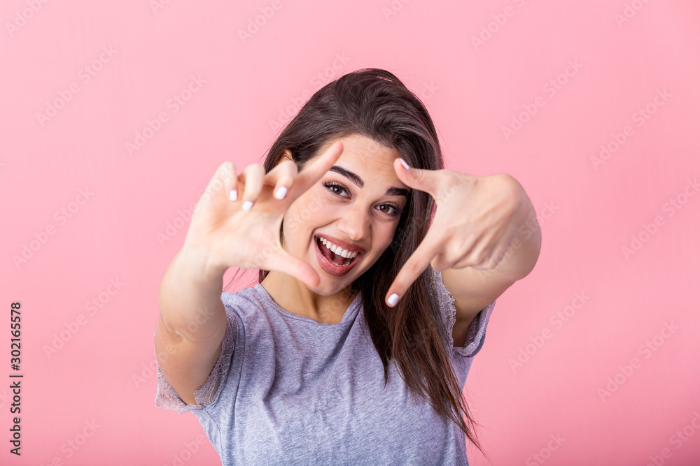 Happy young woman making frame gesture with fingers over pink background. Portrait of a happy smiling woman framing her face with her hands isolated Happy young woman making frame gesture with fingers over pink background. Portrait of a happy smiling woman framing her face with her hands isolated