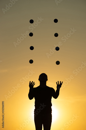 Silhouette of juggler with balls on colorful sunset