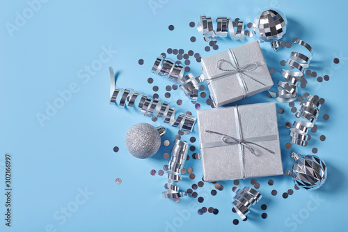 Gift boxes with ribbon and silver christmas decorations on blue background.