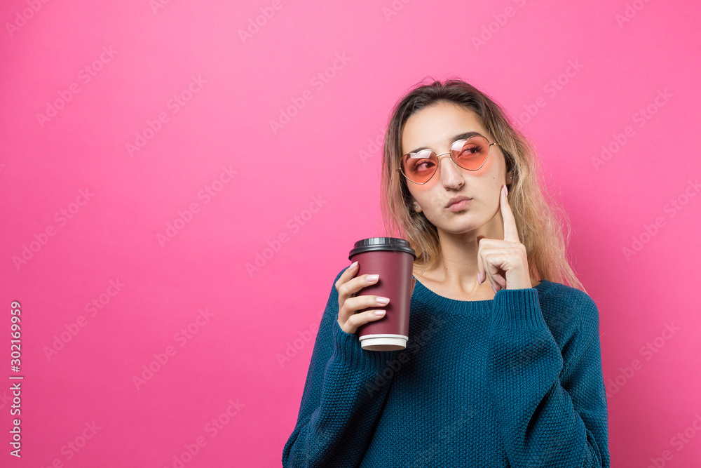 Glamor woman in glasses in a blue sweater with a drink of coffee on a pink background	