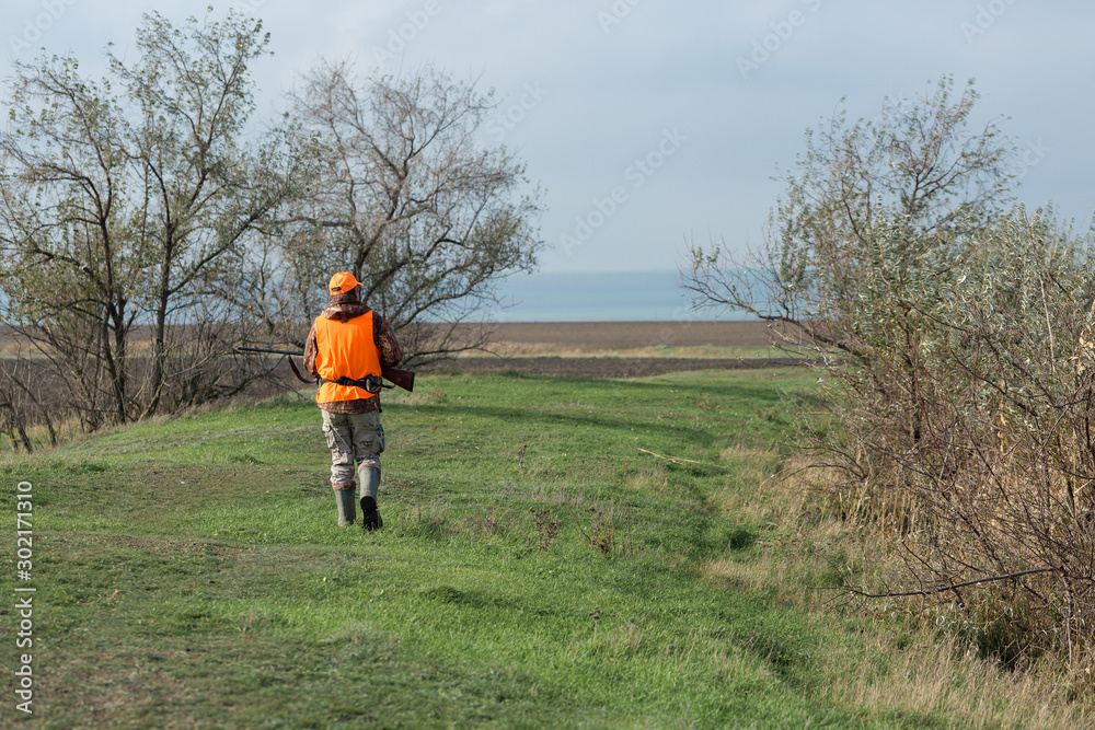 Hunting period, autumn season open. A hunter with a gun in his hands in hunting clothes in the autumn forest in search of a trophy. A man stands with weapons and hunting dogs tracking down the game. Hunting period, autumn season open. A hunter with a gun in his hands in hunting clothes in the autumn forest in search of a trophy. A man stands with weapons and hunting dogs tracking down the game.