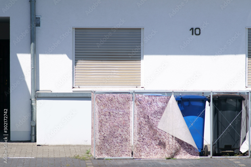 Mülltonnen aus Kunststoff stehen unter einer Metallkonstruktion mit Vorhängen. ..