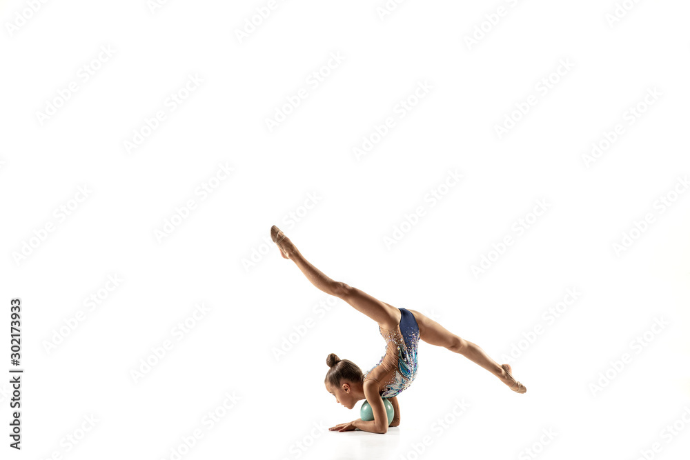 Fototapeta Little flexible girl isolated on white studio background. Little female model as a rhythmic gymnastics artist in bright leotard. Grace in motion, action and sport. Doing exercises with the ball.
