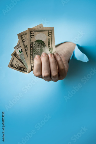 Woman hand with dollars through a hole in paper on blue background